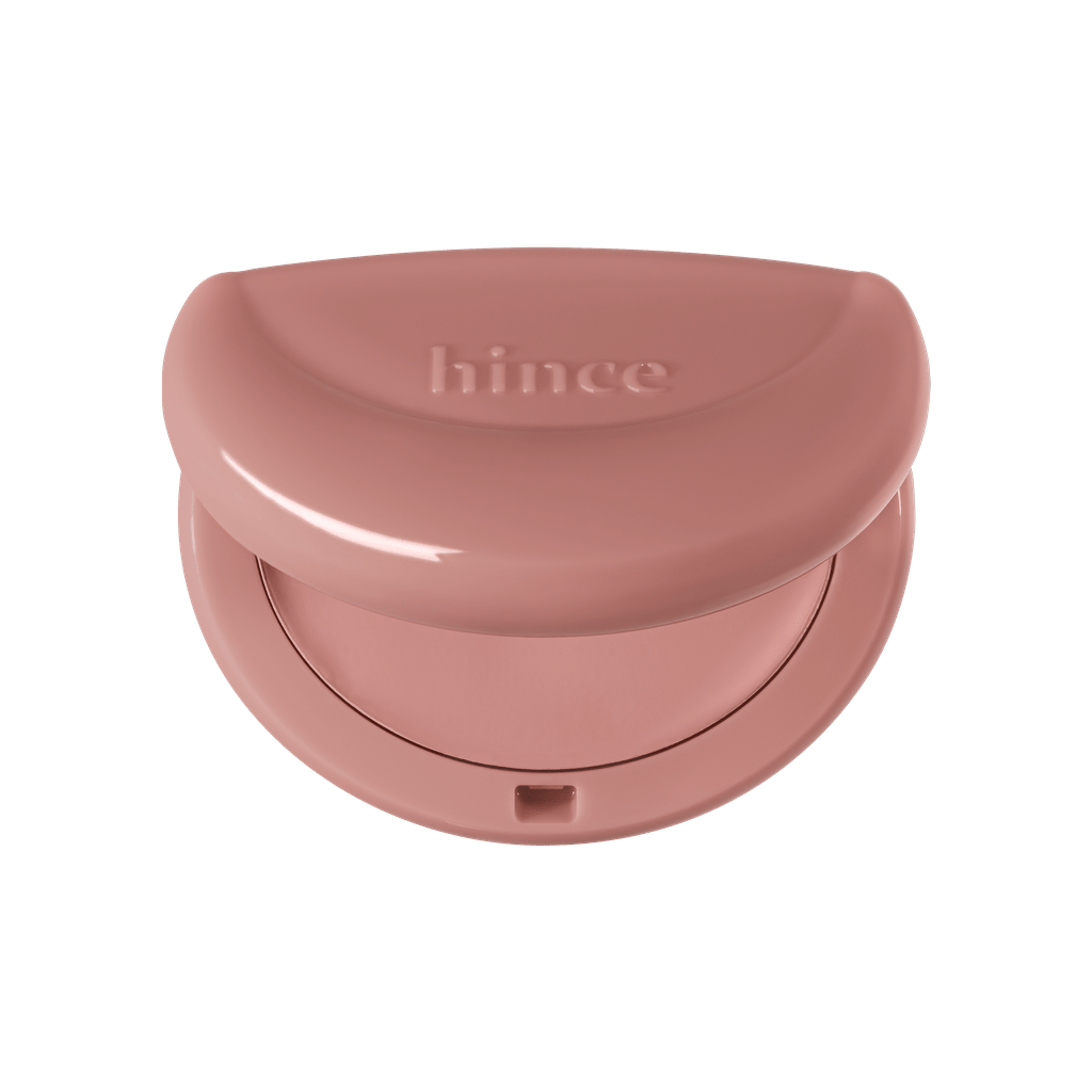 Hince Half-Moon Cheek Cream to Powder Blush in a compact with a half-moon shape and soft pink shade on a mirror surface.